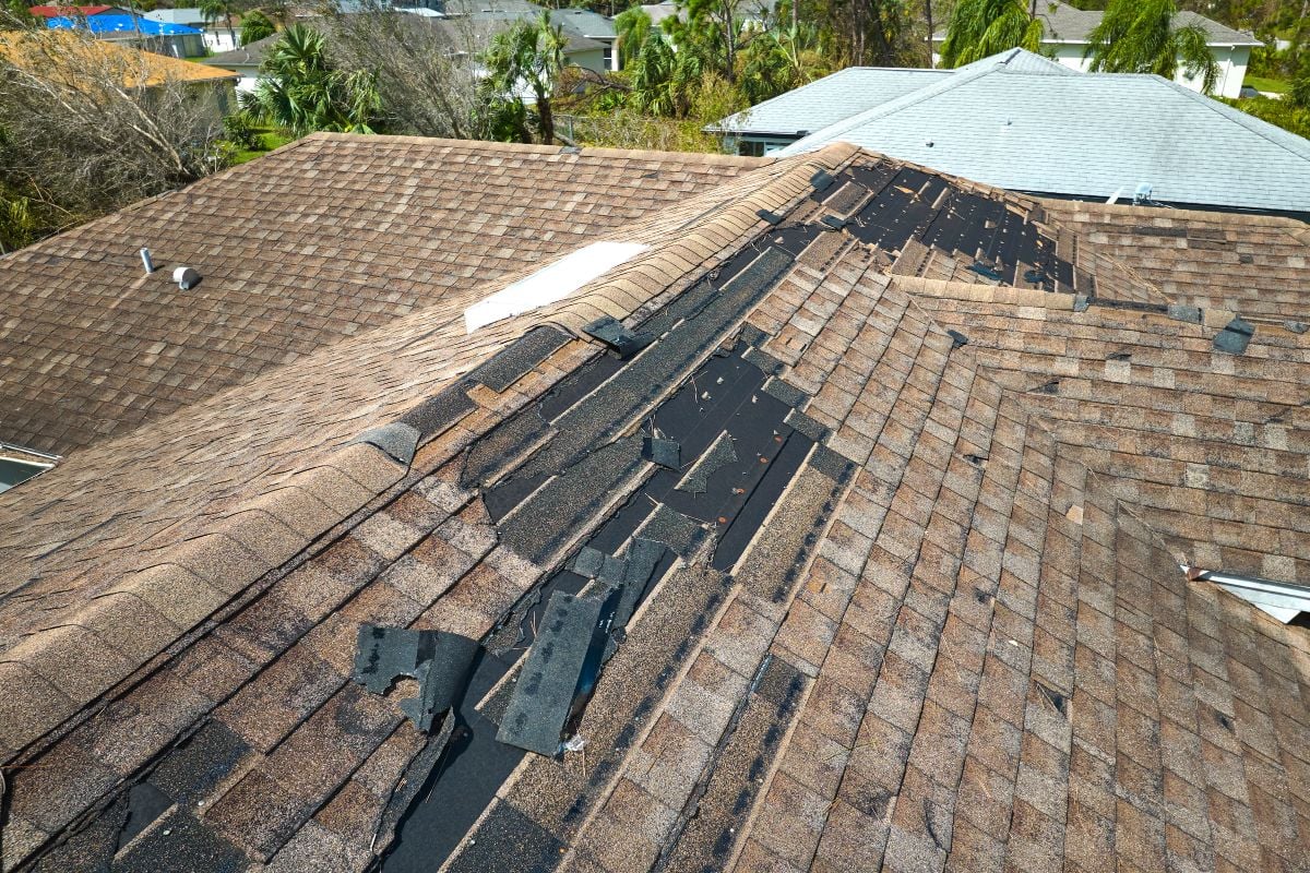 Damaged house roof with missing shingles after hurricane